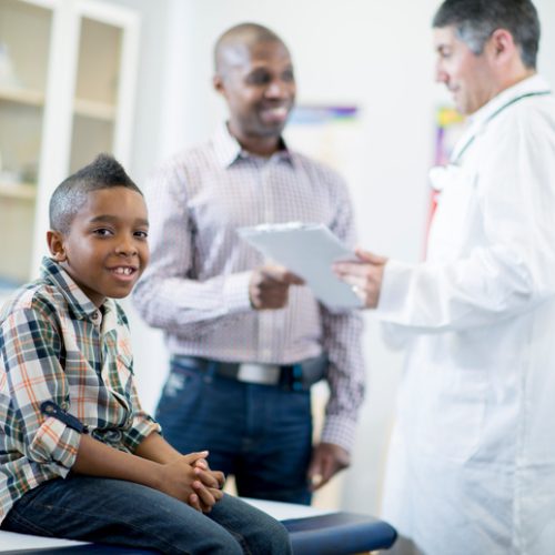 A little boy is at the doctor's office and is getting a check up. He is smiling and looking at the camera.